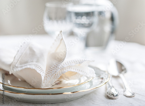 Luxyry dinner set arranged on a table with vintage lace tablecloth and napkins, elegant porcelain dishes, silverware and crystal glassware photo