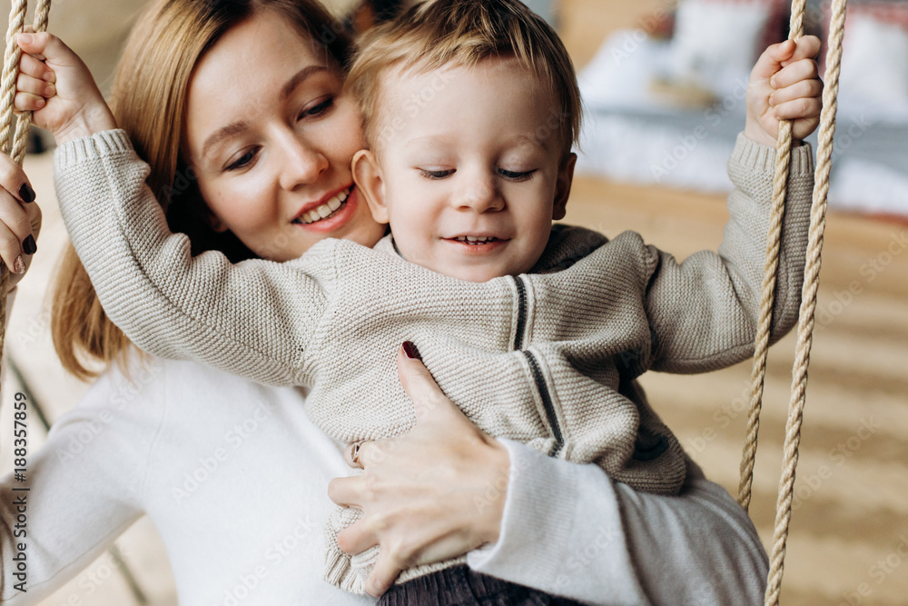 Charming mother has fun with her son playing on the swing in cosy room Charming mother has fun with her son playing on the swing in cosy room