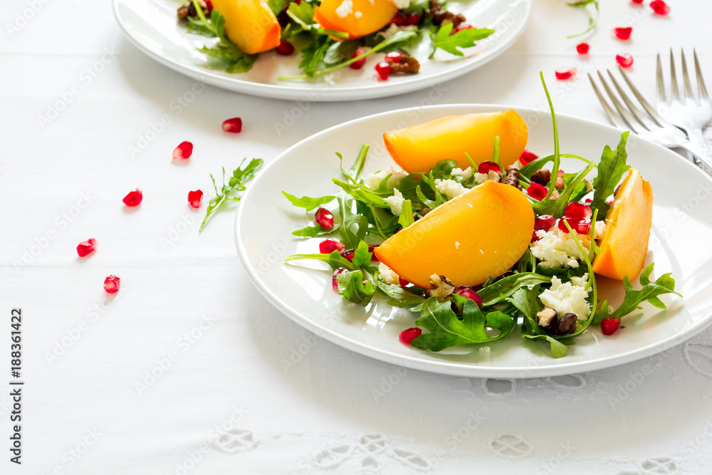 Fresh autumn salad with persimmon, arugula, cheese and pomegranate seeds on white table cloth. Space for copy Fresh autumn salad with persimmon, arugula, cheese and pomegranate seeds on white table cloth. Space for copy
