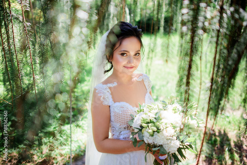 Beautiful bride in a tender dress poses with wedding bouquet in the green forest