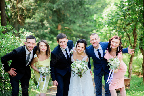 Happy newlyweds and their friends pose in the bright summer park