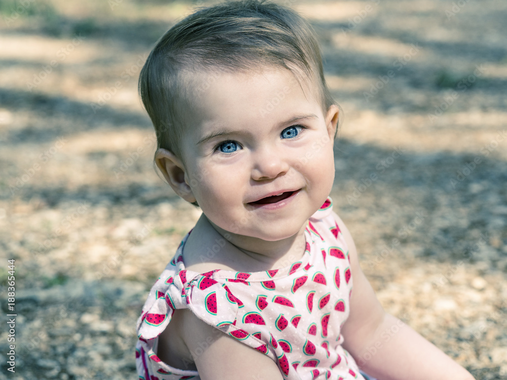 Baby girl looking at camera with expressive blue eyes. She is sitting on the ground. Baby girl looking at camera with expressive blue eyes. She is sitting on the ground.