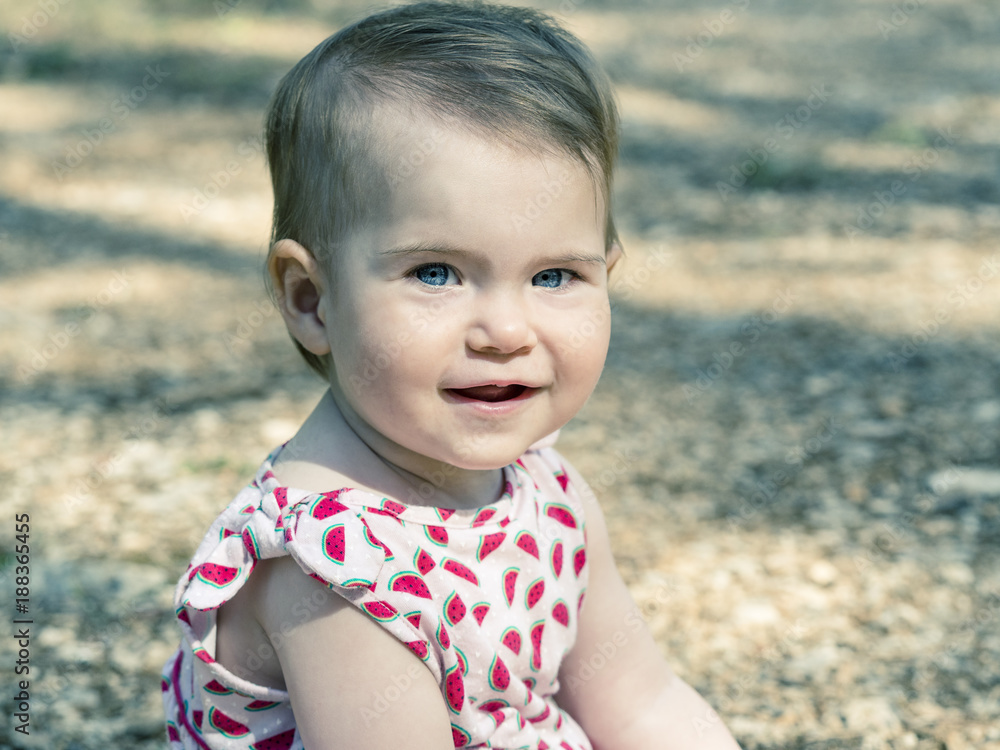 Baby girl looking at camera with expressive blue eyes. She is sitting on the ground. Baby girl looking at camera with expressive blue eyes. She is sitting on the ground.
