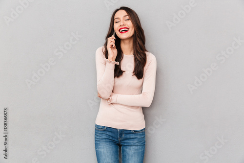 Portrait of pretty smiling woman with brown hair talking on mobile phone having pleasant conversation over gray background