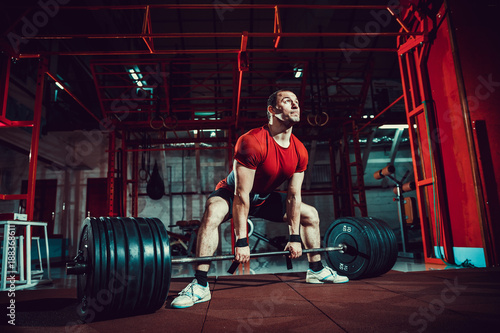 Muscular fitness man doing deadlift a barbell in modern fitness center. Functional training. Snatch exercise. Sumo style. photo