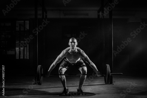 A muscular man squats with a barbell in the gym. Black and white photo