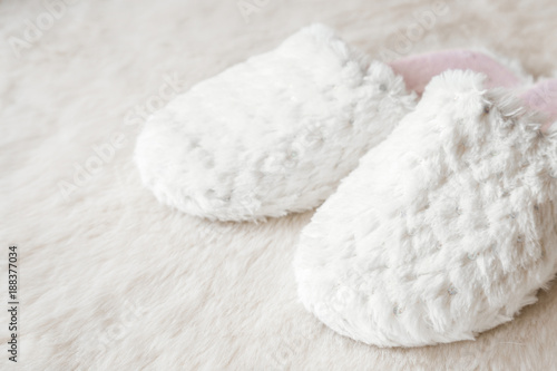 Beautiful, soft, warm slippers waiting an owner on the white fluffy mat in the bedroom in the morning. Comfortable home shoes concept.