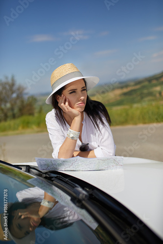 Young woman got lost in the field while driving a car and reading paper map