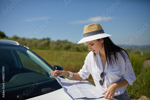 Young woman got lost in the field while driving a car and reading paper map