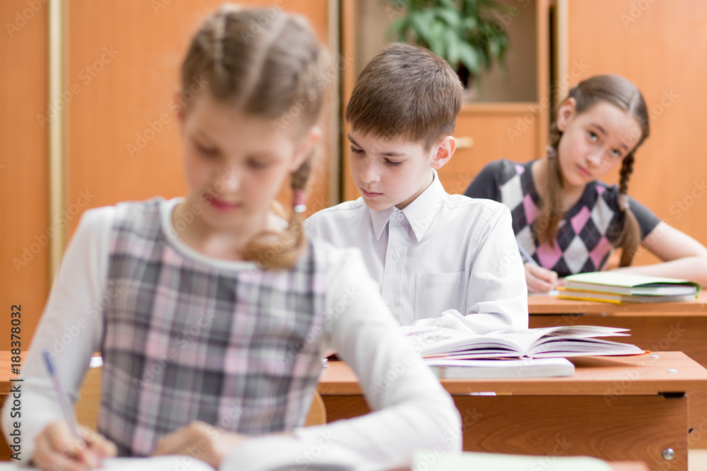 Education, school, learning and children concept - group of school kids with pens and textbooks writing test in classroom Education, school, learning and children concept - group of school kids with pens and textbooks writing test in classroom