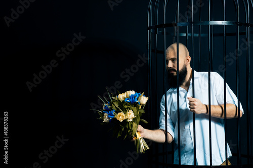 bearded man holding out a bouquet with flowers. The brutal man in the cage over black background photo