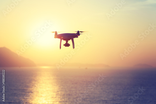 silhouette of flying drone which taking photo over sunrise sea.
