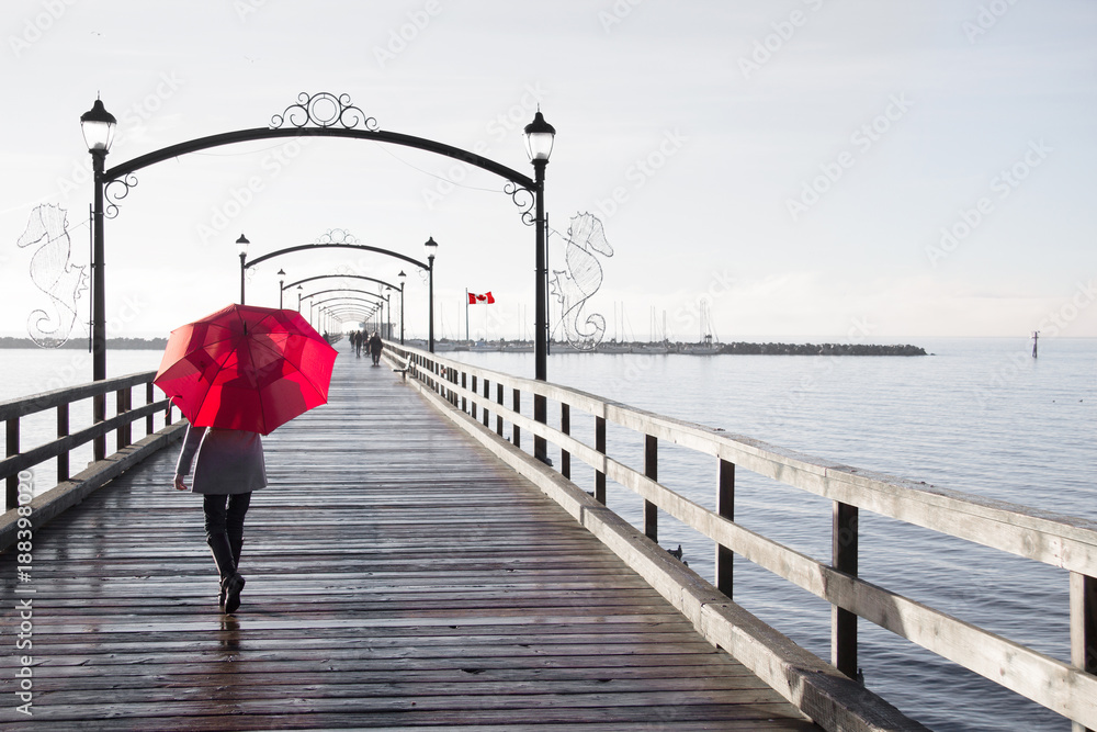 Woman holding a red umbrella walking on a rainy day on the pier in White  Rock, British Columbia, Canada. A Canadian flag is visible in the  background. Stock Photo | Adobe Stock