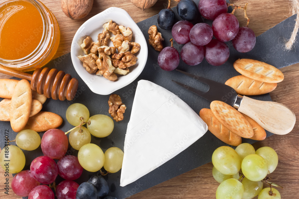 Cheese plate with Brie / Cheese Brie with grapes, walnut, honey in jar, crackers on slate board and wooden background Cheese plate with Brie / Cheese Brie with grapes, walnut, honey in jar, crackers on slate board and wooden background