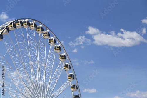 Giant Ferris wheel with numbered cabins in the park - Bright blue sky with sharp clouds behind it.