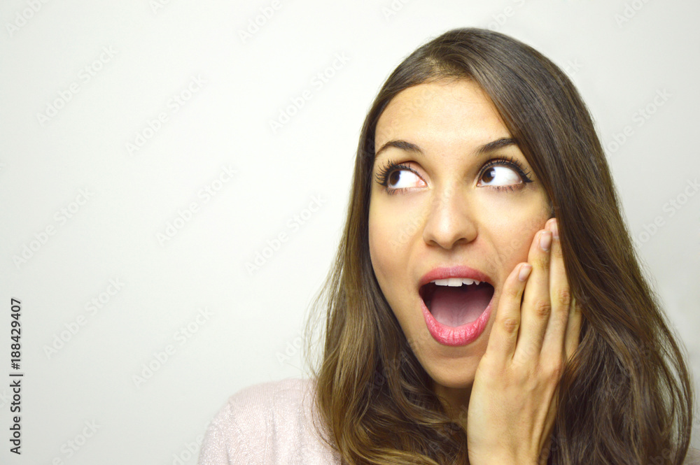 Surprised young woman looking to the side with open mouth with hand on the face on white background. Excited girl looking to the side your product or brand. Copy space. Surprised young woman looking to the side with open mouth with hand on the face on white background. Excited girl looking to the side your product or brand. Copy space.
