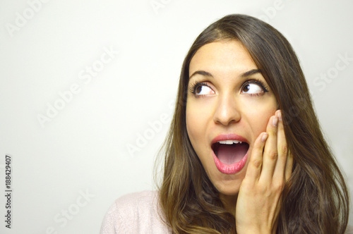 Surprised young woman looking to the side with open mouth with hand on the face on white background. Excited girl looking to the side your product or brand. Copy space.
