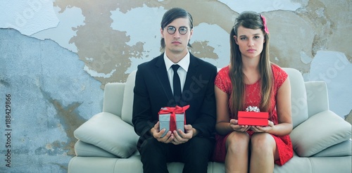 Composite image of unsmiling geeky couple with gift photo