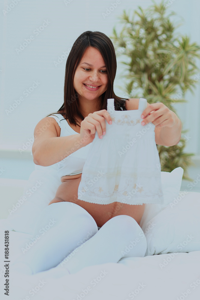 Pregnant woman contemplates the future baby dress. Pregnant woman contemplates the future baby dress.