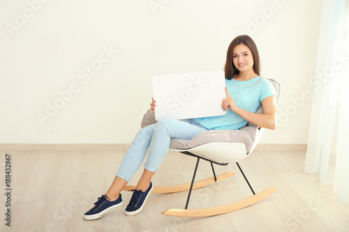 Young woman with blank advertising board indoors