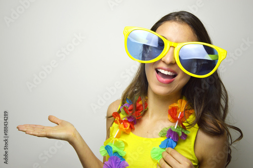 Carnival time. Young woman with big funny sunglasses and carnival garland smile at camera and show your product or text on gray background.