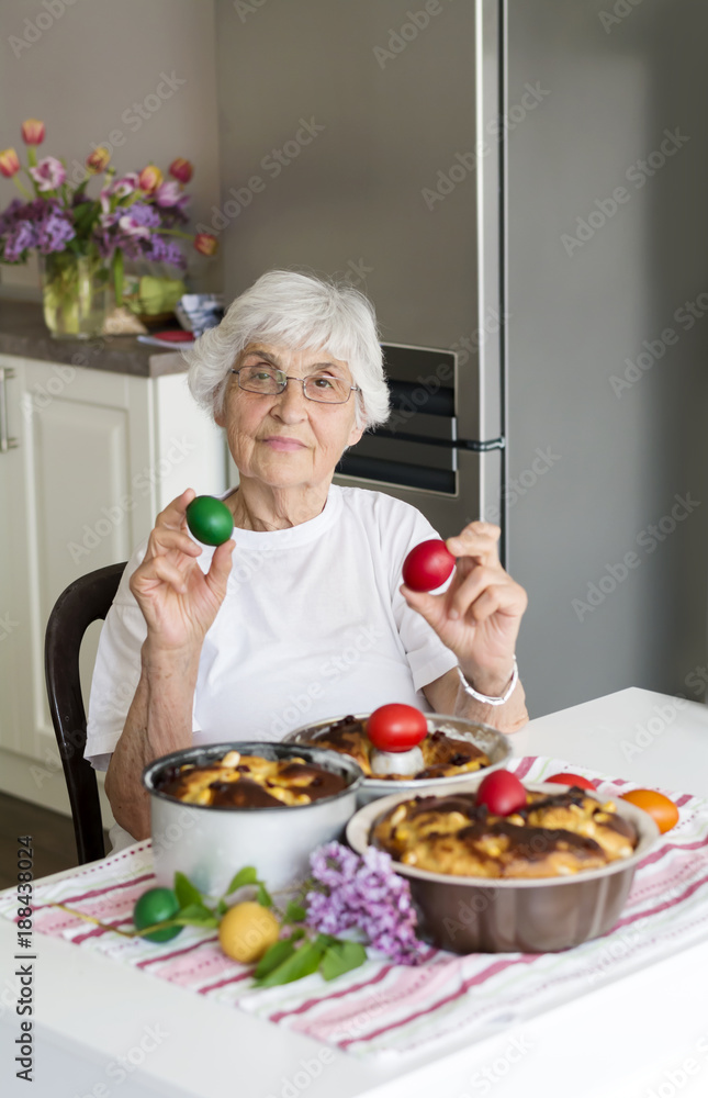 Beautiful Senior Woman with Easter Eggs and Easter Breads on the Table at Home.Selective focus Beautiful Senior Woman with Easter Eggs and Easter Breads on the Table at Home.Selective focus