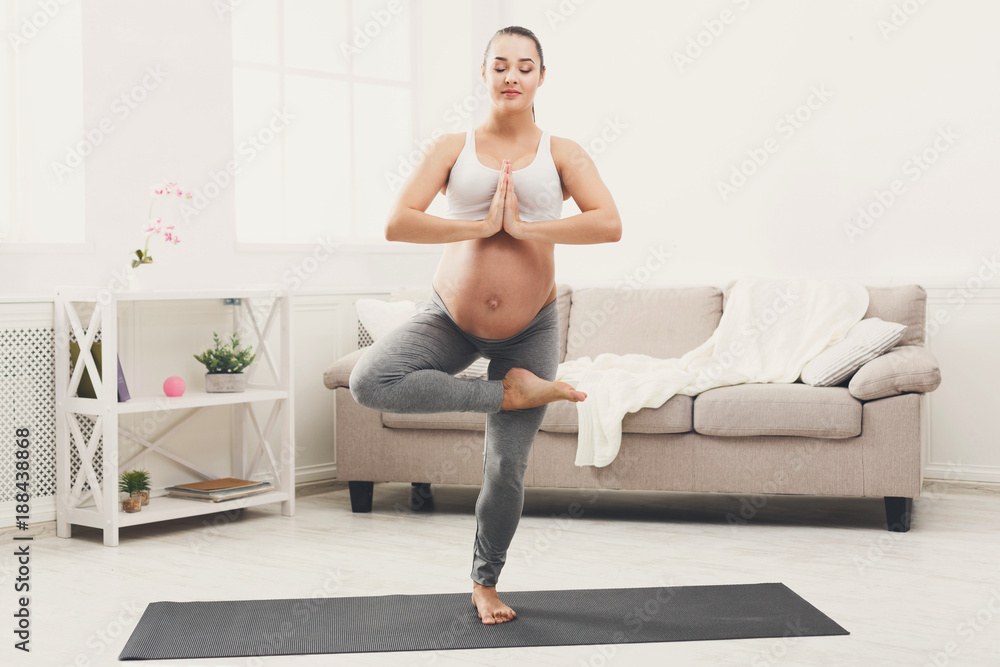 Happy pregnant woman training yoga in tree pose