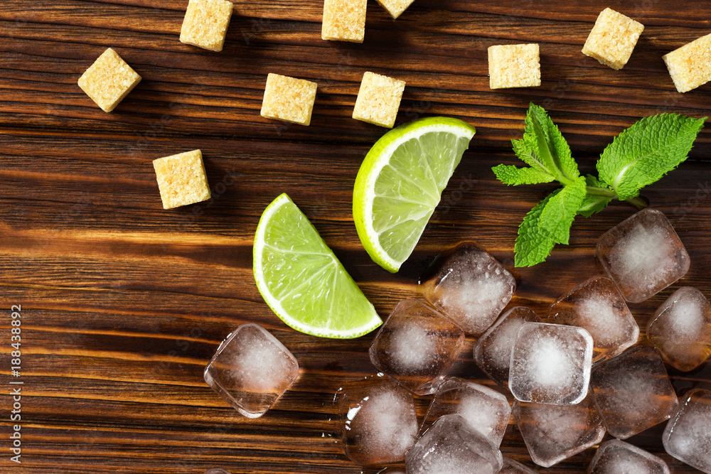 Ingredients for mojito on a wooden brown background. Ice cubes, mint, lime and sugar cane Ingredients for mojito on a wooden brown background. Ice cubes, mint, lime and sugar cane
