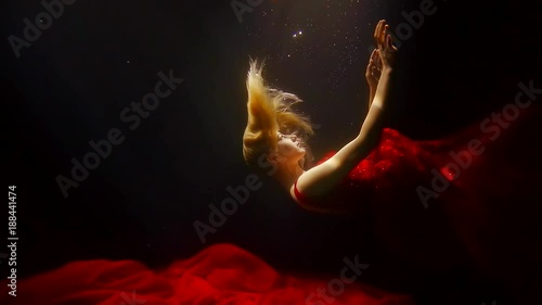 elegant slim woman is falling to the sea bottom in dark water, she is pushing off with her hands photo