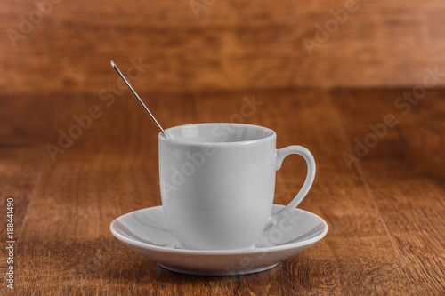 white coffe Cup with spoon on white saucer on dark brown wooden background