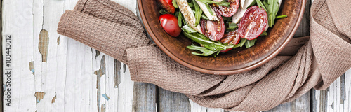 Closeup of delicious salad of arugula with cherry tomatoes and chicken breast in a clay bowl on a wooden table, top view. Sports nutrition. Balanced meals.