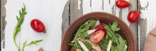 Closeup of delicious salad of arugula with cherry tomatoes and chicken breast in a clay bowl on a wooden table, top view. Sports nutrition. Balanced meals.