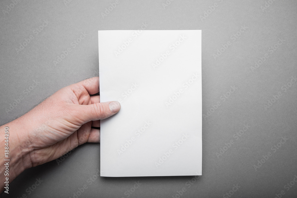 Fototapeta premium Blank sheet A5 for design, a mock-up in the hand of a European man.