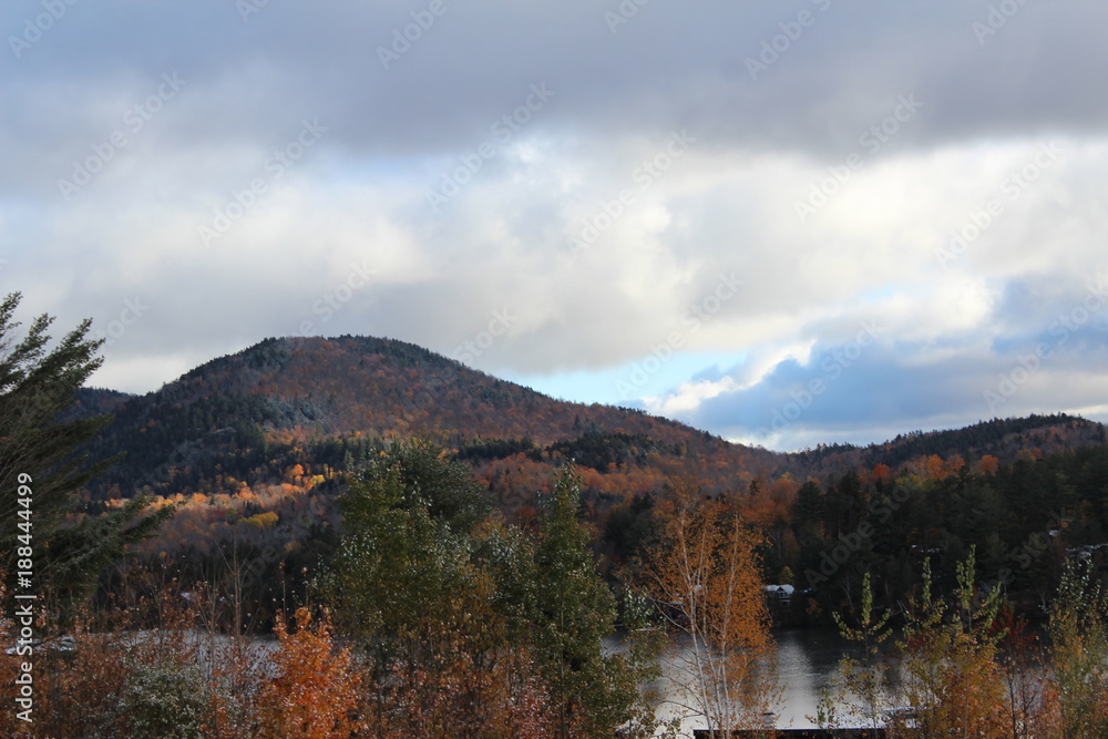 autumn mountain view with light snow on trees, near lake, and clouds above mountains