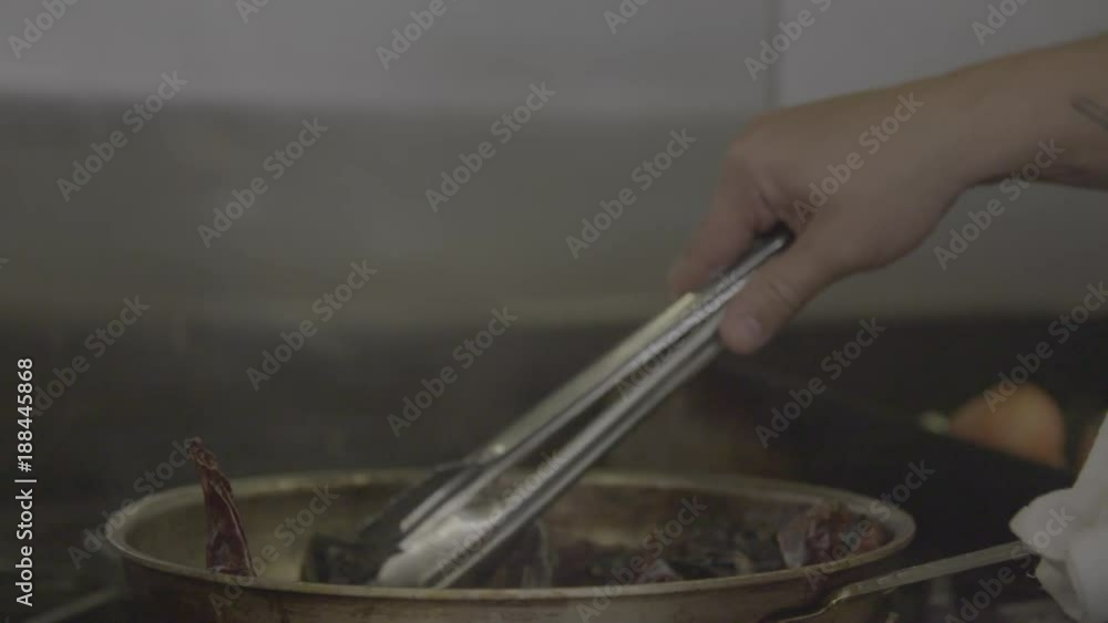 Chef uses tongs on dried chili peppers in pan, close up Chef uses tongs on dried chili peppers in pan, close up