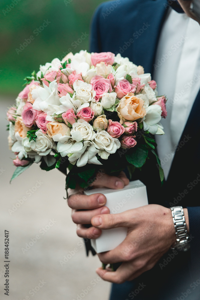 fiance in a dark blue suit holds a wedding bouquet made of white flowers fiance in a dark blue suit holds a wedding bouquet made of white flowers