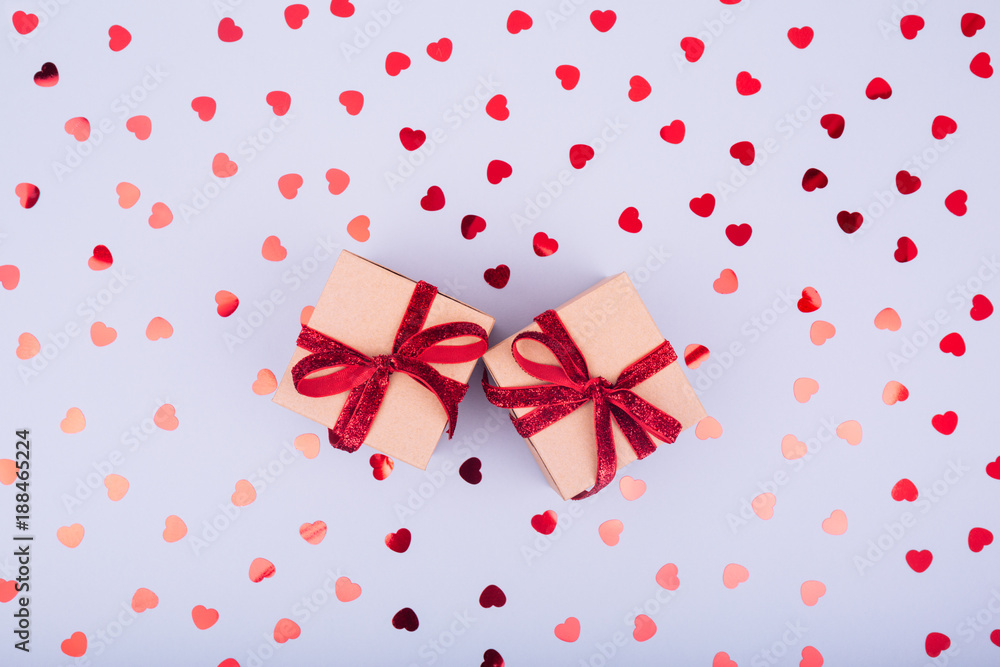 Craft box with red ribbon bow and glitter heart confetti. Valentine day concept. Trendy minimalistic flat lay design background Craft box with red ribbon bow and glitter heart confetti. Valentine day concept. Trendy minimalistic flat lay design background