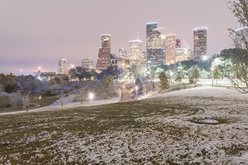 Downtown Houston at  twilight with big and fluffy snowflakes fell on meadow grass at Eleanor Tinsley Park. Park lawn, curved bike pathway, modern skylines in background. Snow is extremely rarely here