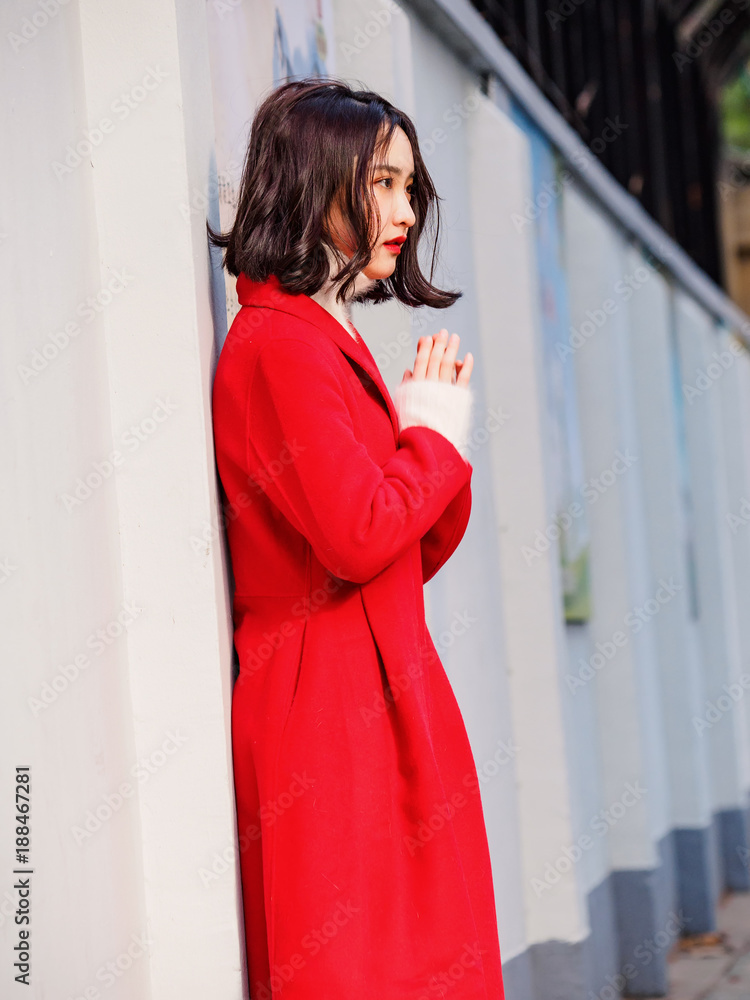 Fototapeta premium Beautiful young brunette woman wearing a red coat in autumn city. Outdoor fashion portrait of glamour young Chinese cheerful stylish lady in street. Emotions, people, beauty and lifestyle concept.