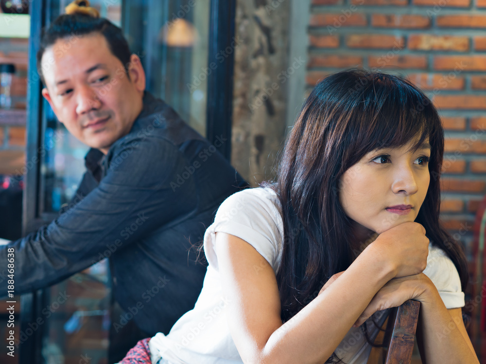 Asian young man and woman feeling upset after quarrel and broken heart, waiting to say sorry in coffee shop on dating 