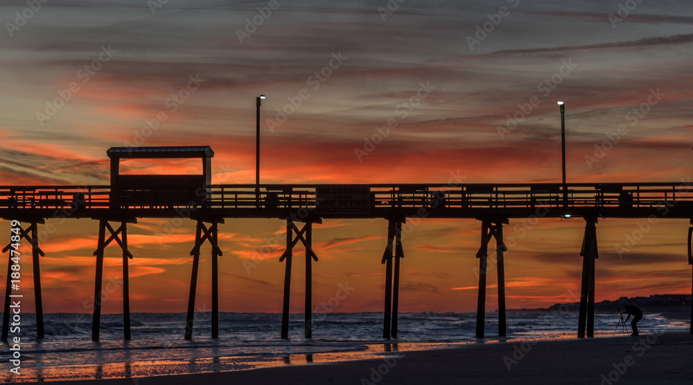Colorful Sunset at ocean coast with silhouette of pier and photographer