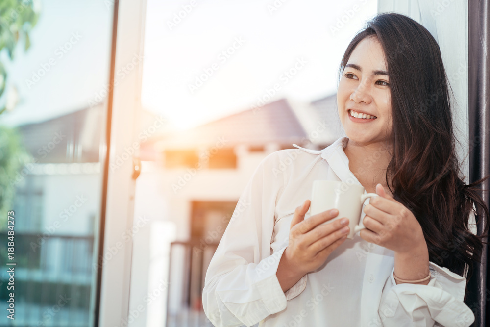 Asian girl who just wake up in the morning as relaxed. She opened the window to receive the light of the morning sun. She was holding a cup of coffee or tea to drink it. Asian girl who just wake up in the morning as relaxed. She opened the window to receive the light of the morning sun. She was holding a cup of coffee or tea to drink it.