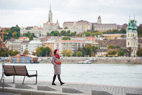 Photography A stylish girl walks along the embankment of Budapest with blurred view of Buda side of Budapest with the Buda Castle, St