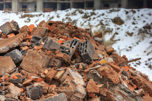 A pile of construction debris with broken bricks and concrete in winter against a background of snow.