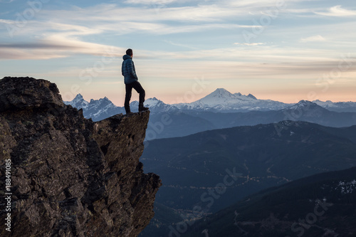 Fotografie Adventurous man on top of the mountain during a vibrant sunset