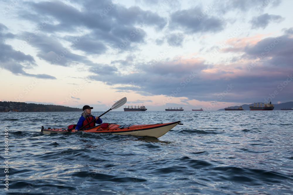 Adventurous girl kayaking on a sea kayak during cloudy Sunrise. Taken in Vancouver, BC, Canada. Adventurous girl kayaking on a sea kayak during cloudy Sunrise. Taken in Vancouver, BC, Canada.