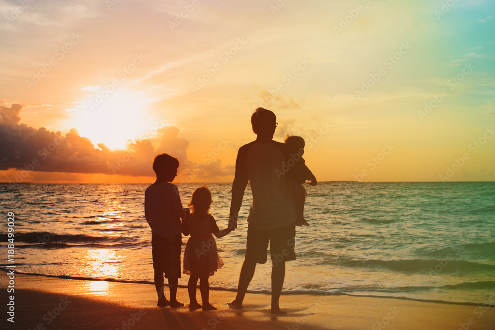 father with three kids walking on beach at sunset