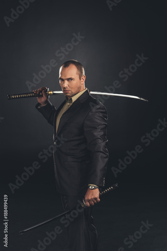 handsome man in suit with katana sword isolated on black photo