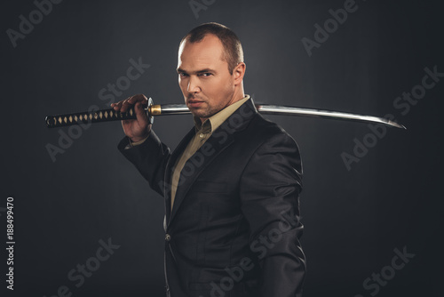 serious man in suit with katana sword isolated on black