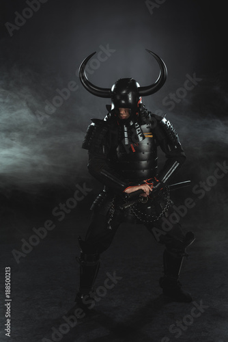 armored samurai taking out his katana on dark background with smoke